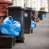 Black wheelie bins and blue recycling bags lined up along a pavement on a residential street.