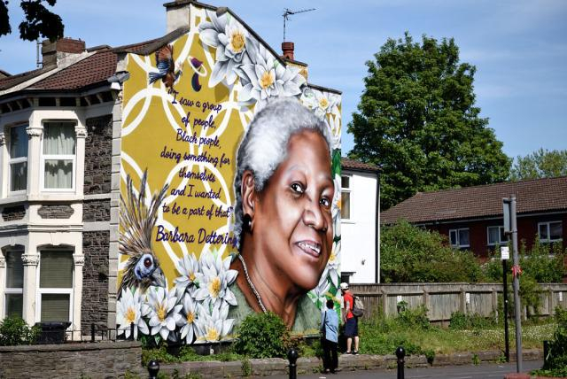 A large mural of a white haired older black woman on side of a house.