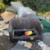 An old sofa that has been dumped with other household waste including mattresses