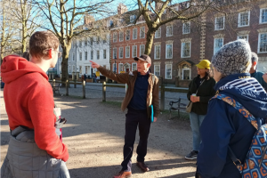 A group of people stand on Queen's Square in Bristol listening to a tour guide.