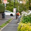 Photograph of the back of a cyclist on a cycle lane at a junction with a road with a white car travelling along it.