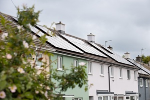 Row of pastel-coloured terraced houses with solar panels installed on the roofs.