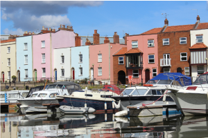 Narrow boats moored up at the harbourside with colourful tall houses in background.
