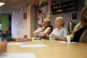 People seated at a table in a community room with papers, cups, and bunting overhead