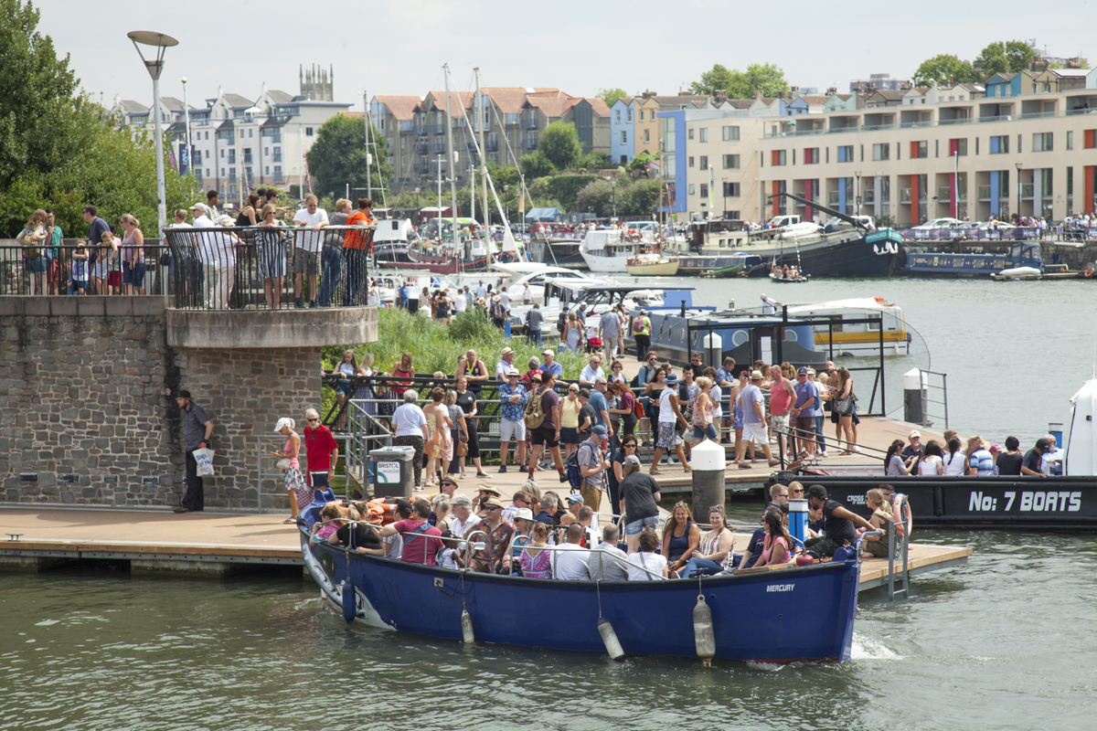 Lots of people in a boat on the water, some more boats and people in the background