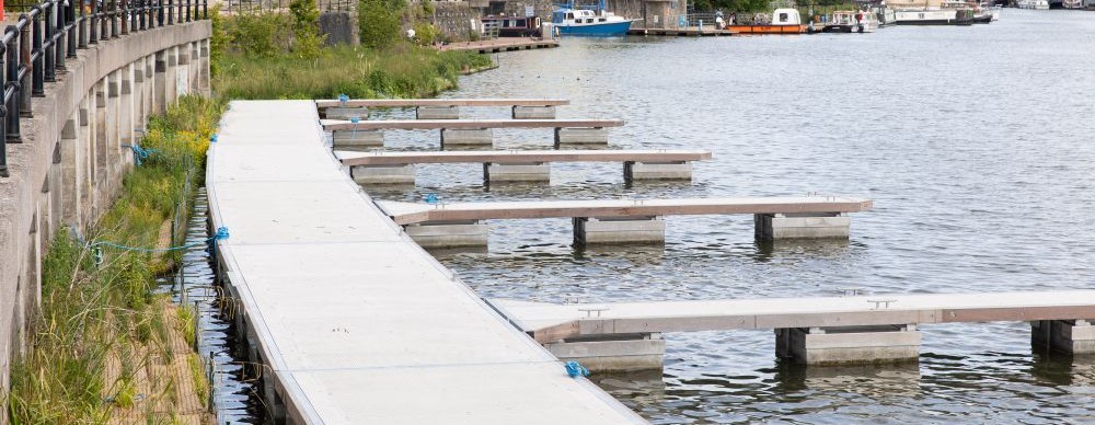 Some mooring platforms on the harbour, water in the background and some buildings