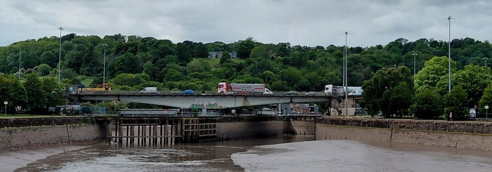A river with a bridge at the end that's been taken apart. A bridge going over the river with a lorry on it.