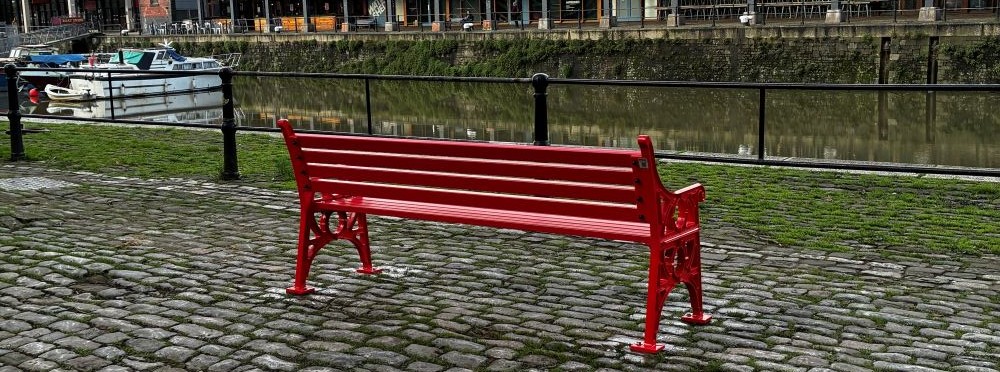 A red bench overlooking the harbour, boats in the background