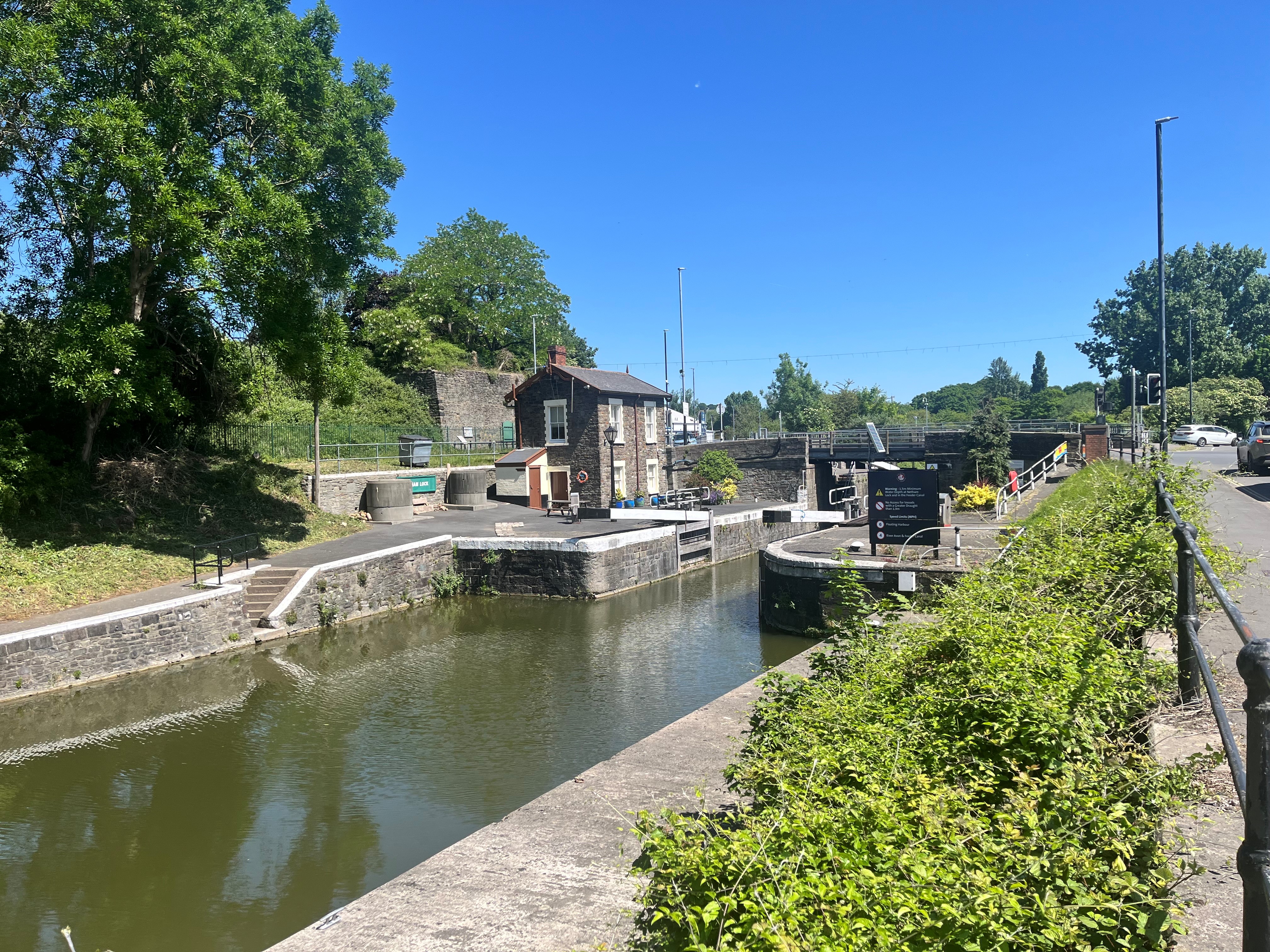The river running past a small house on the left and some bushes on the right, blue skies