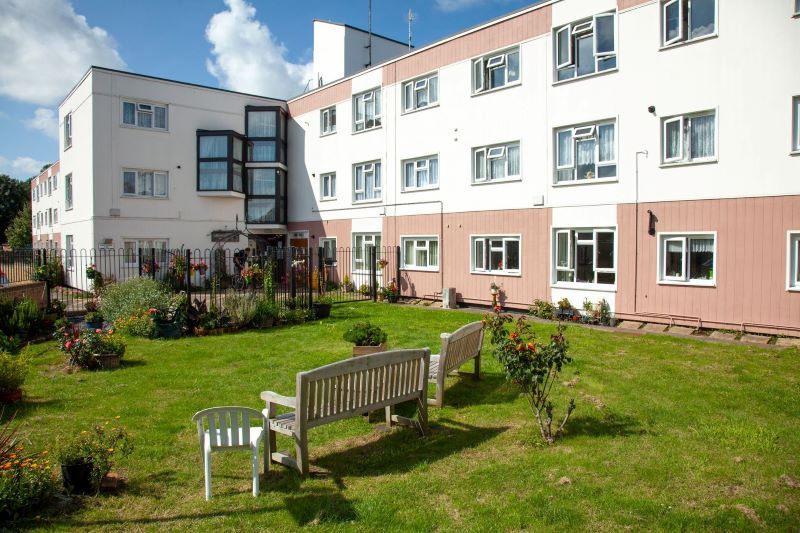 a block of white and pink council flats with a green area and white benches in the foreground