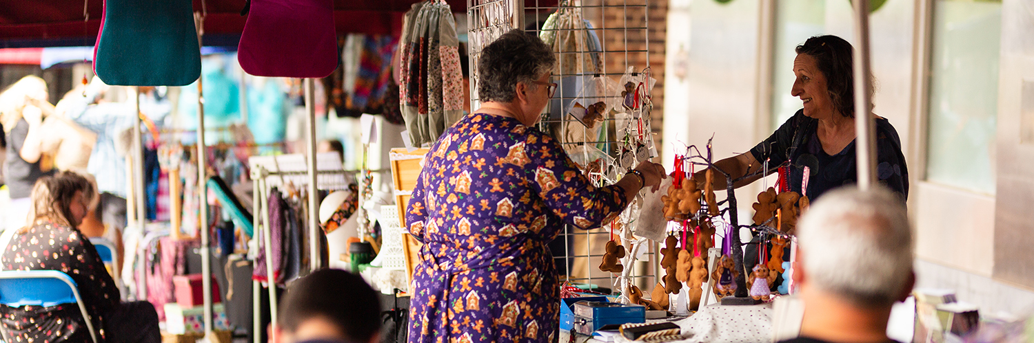 A woman tells another woman about a product she's selling at her market stall