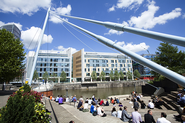 People sitting by the river near Bristol Temple Meads station looking across at large office buildings