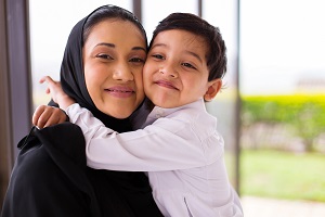 A woman in a headscarf and a young boy hugging and smiling