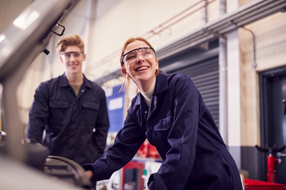 A couple of young people in overalls and wearing safety goggles in a workshop.