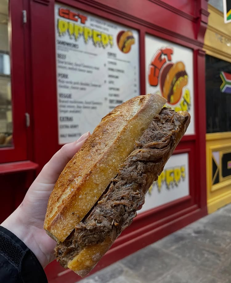Someone holding a baguette filled with brisket meat in front of the Get Dipped stall