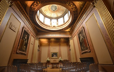 A high ceilinged room with period panelling and two sets of three rows of chairs