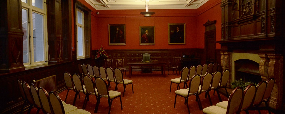 a high ceilinged room with rows of chairs facing a desk at the front of the room 